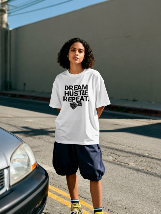 Person wearing a white t-shirt with 'Dream Hustle Repeat' text in an urban setting.