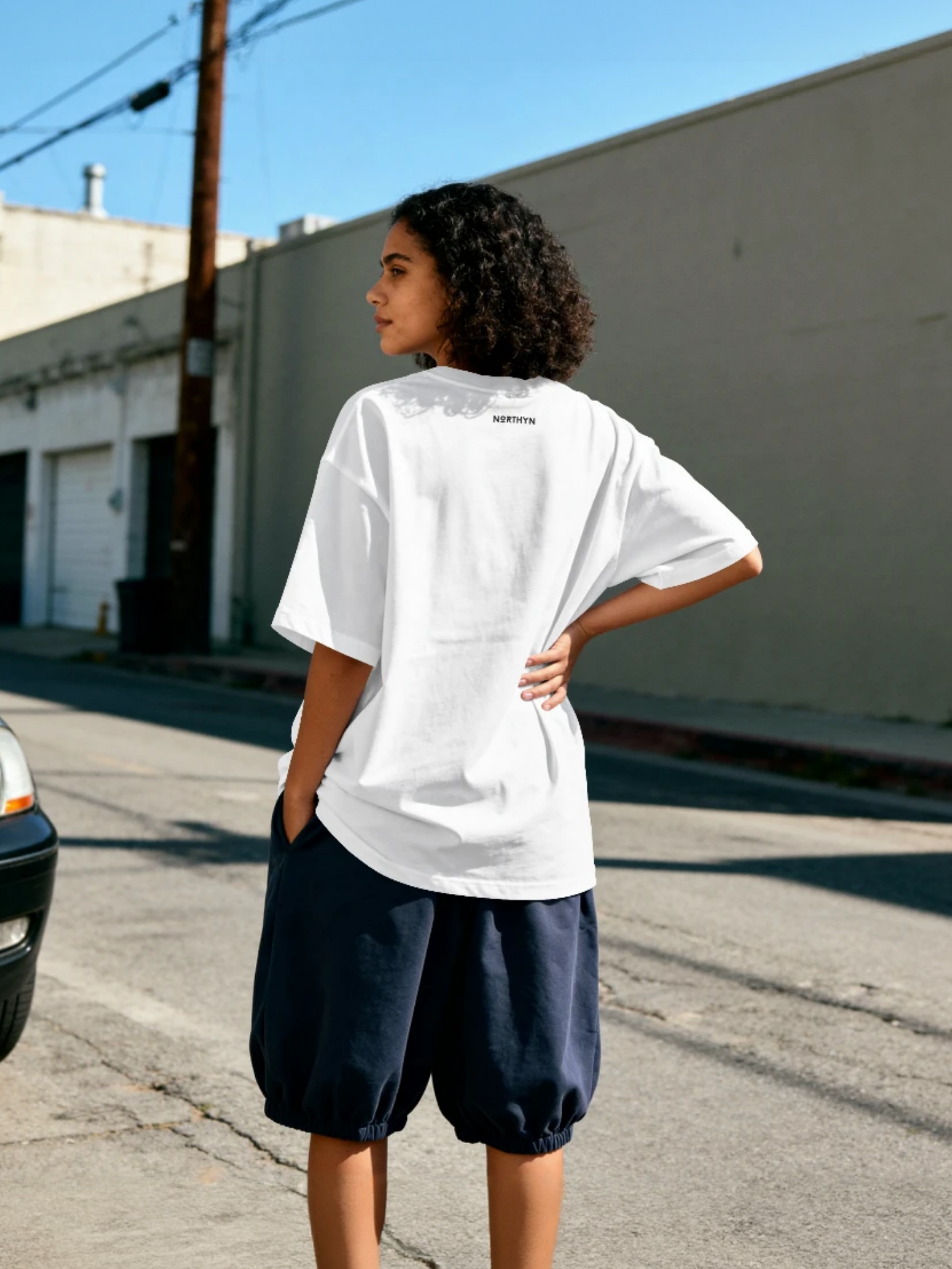 Person wearing an oversized white t-shirt and navy shorts standing on a street.